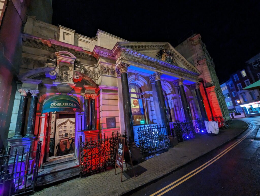 An external shot of the Old India restaurant in Bristol. The columns of the facade are lit up with blue and red lights